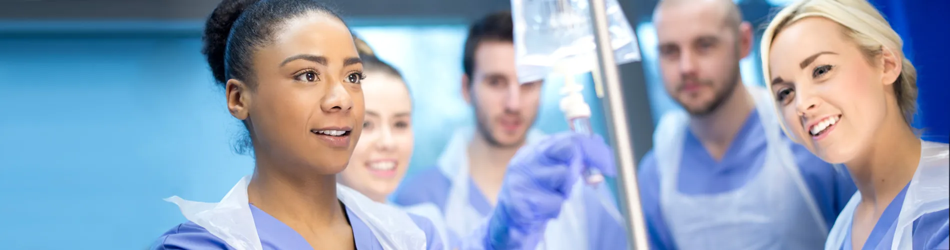 Nurse setting up an IV drip with more nurses in the background.