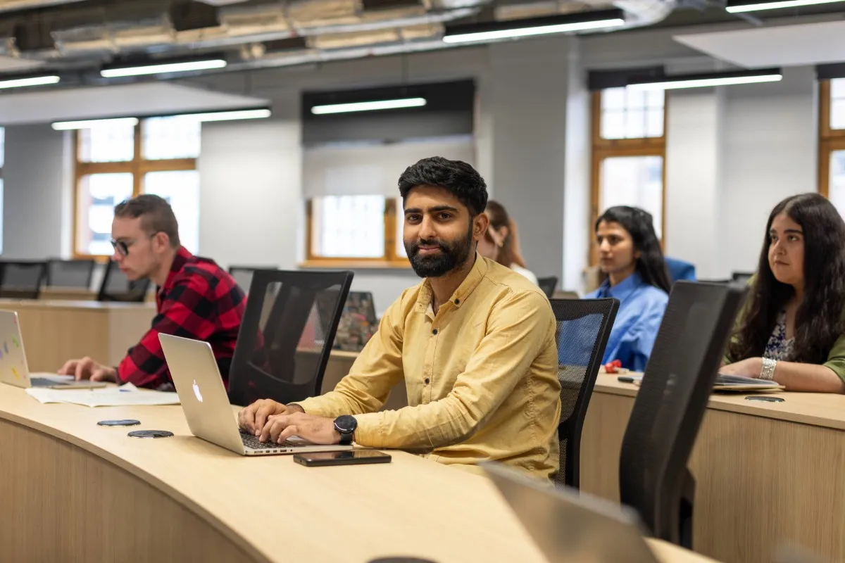 Digital Marketing students listening to lecture in lecture theatre at Leeds City Campus. One student working on laptop and looking at the camera..