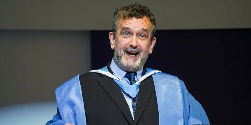 A university professor dressed in blue and black academic gown and speaking at a lecture..