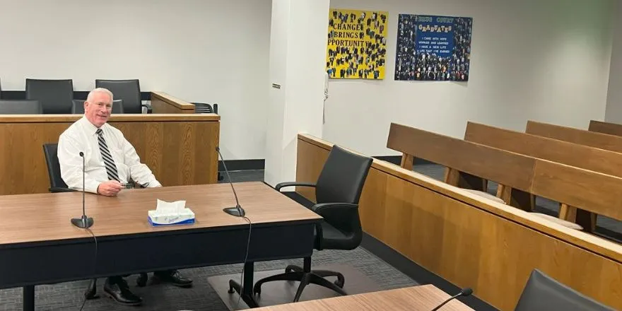 A man wearing a white shirt and black tie sits in a drug court.