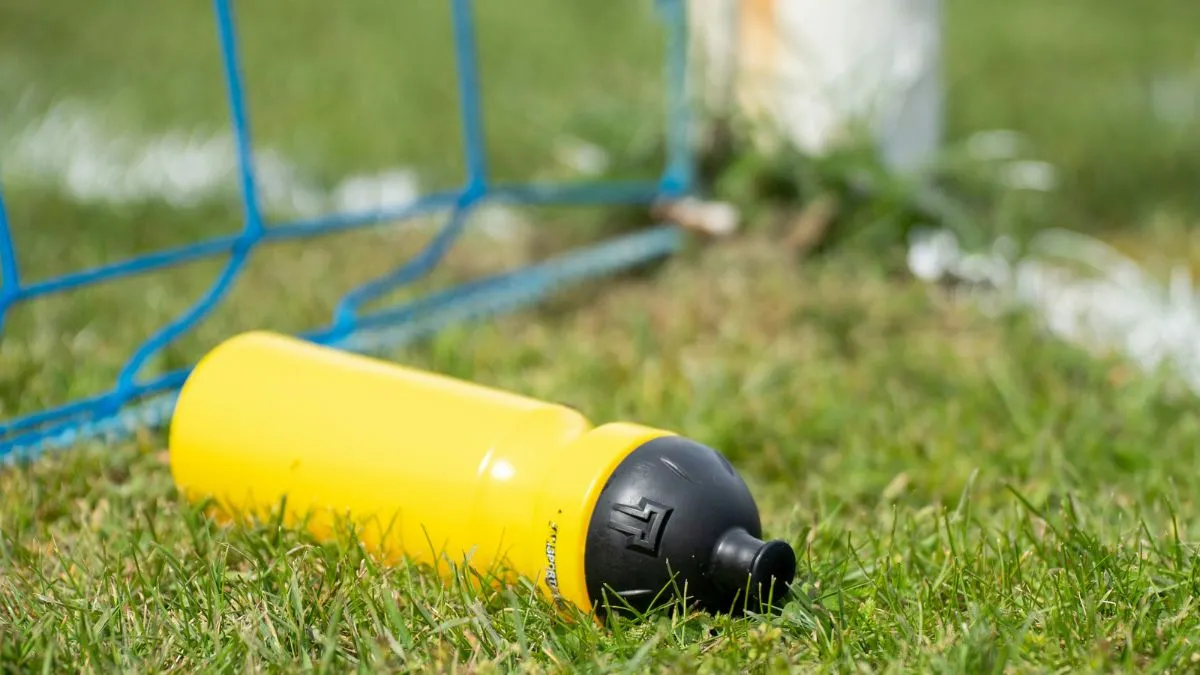 A water bottle on the grass next to a football goal.