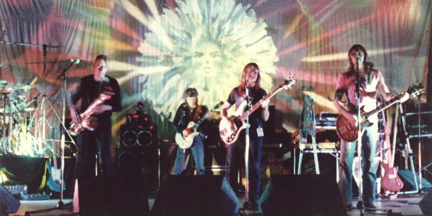 Four men on stage with guitars and microphones.