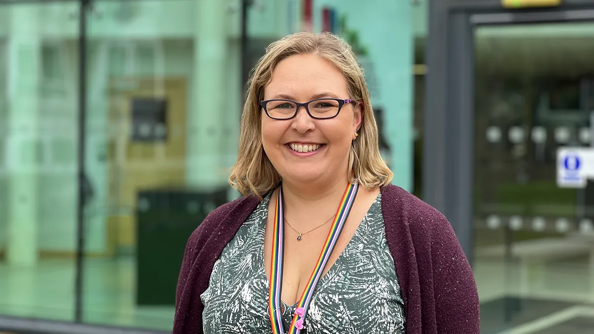 An academic smiling outside the Leeds Trinity University reception building..