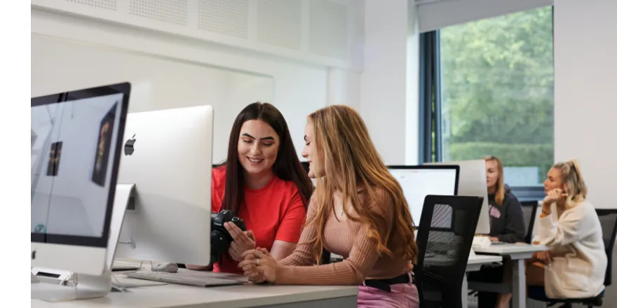 Students sat at computer looking at digital camera.