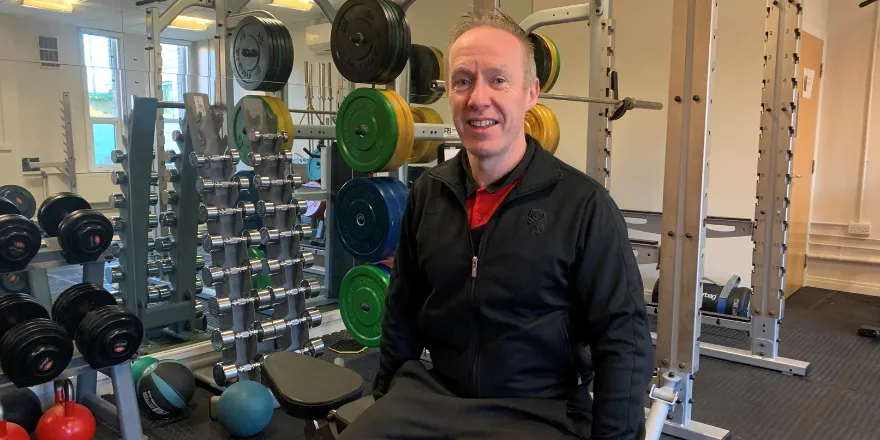 Male lecturer smiles in weight section of gym.