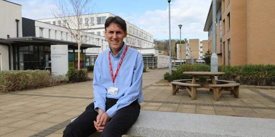A man sat on a bench outside university building.