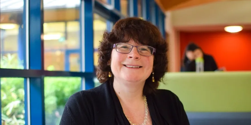 Woman with brown hair, glasses and wearing black jacket.