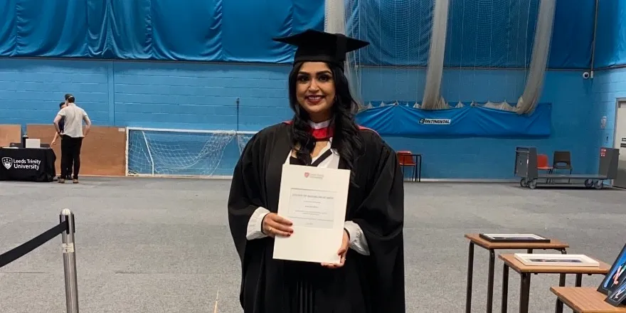 Female student with dark hair in black cap and gown holding degree certificate.