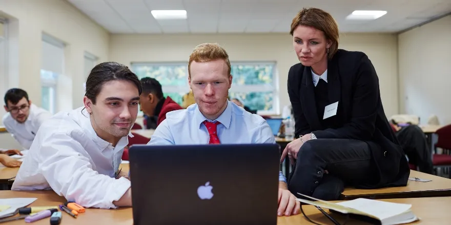 Two males and one female looking at black Macbook.