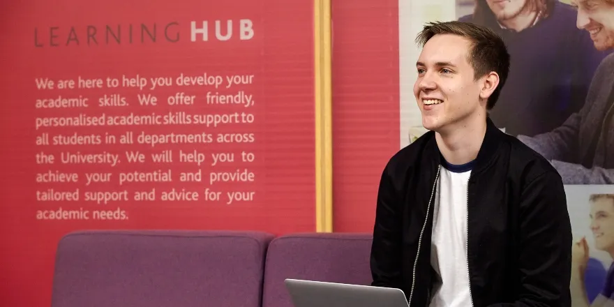blonde man with silver laptop on purple sofa.
