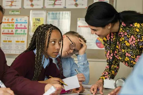 Primary school students working with their teacher at a desk.