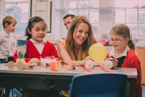Young female teacher interacting with primary school students in a classroom setting. .