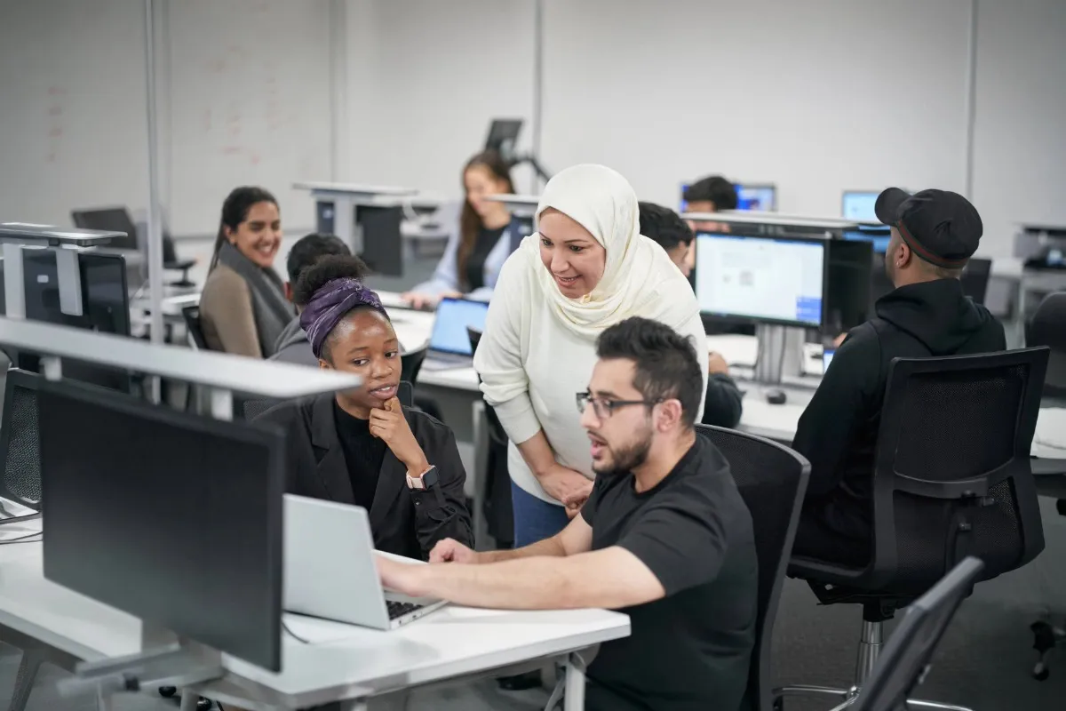 Two students using computer and lecturer helping.