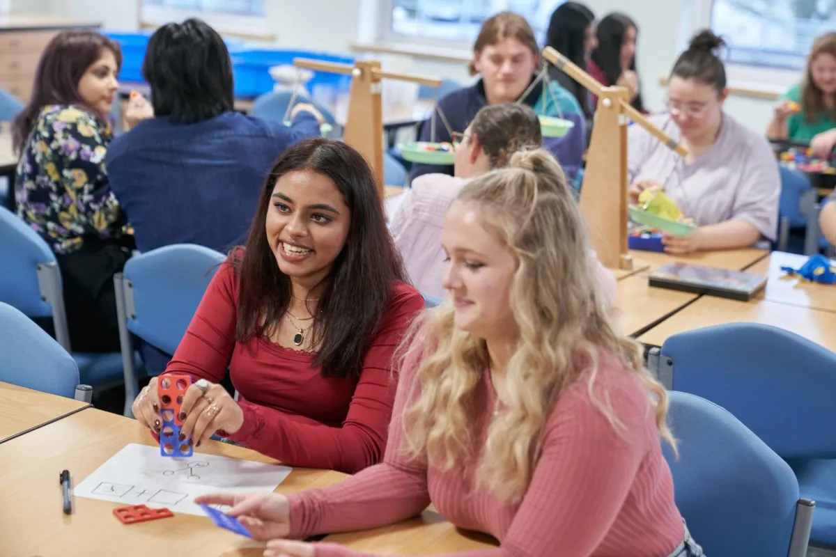 People sit at tables in a classroom using colourful educational materials during a hands‑on learning activity.