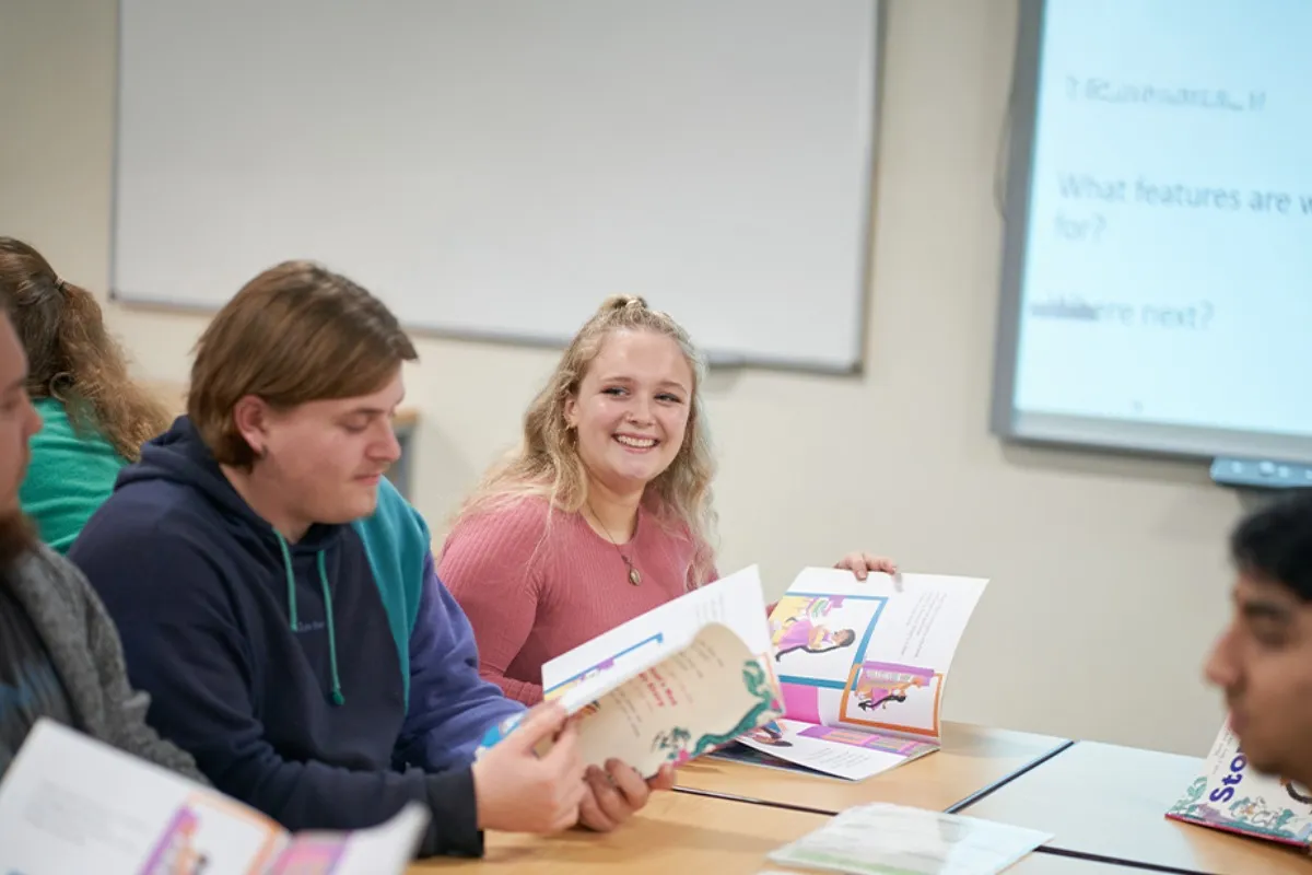 People sit at a classroom table holding colourful booklets.