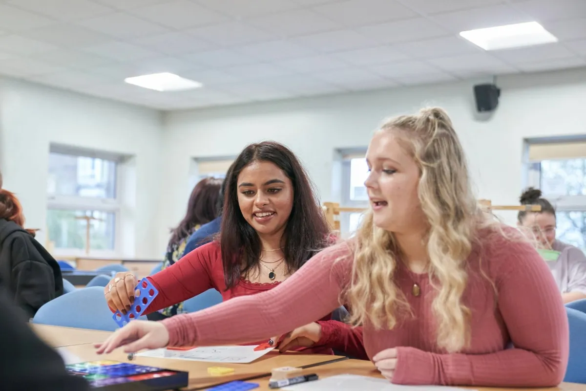 Two people sit at a classroom table using colourful counting blocks during a learning activity.