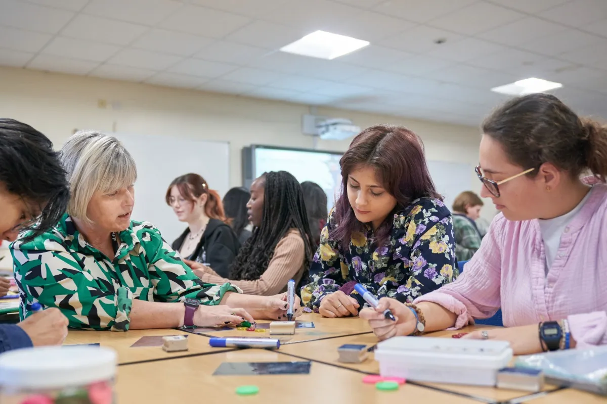People sit together at a table working with colourful counters and materials during a classroom activity.