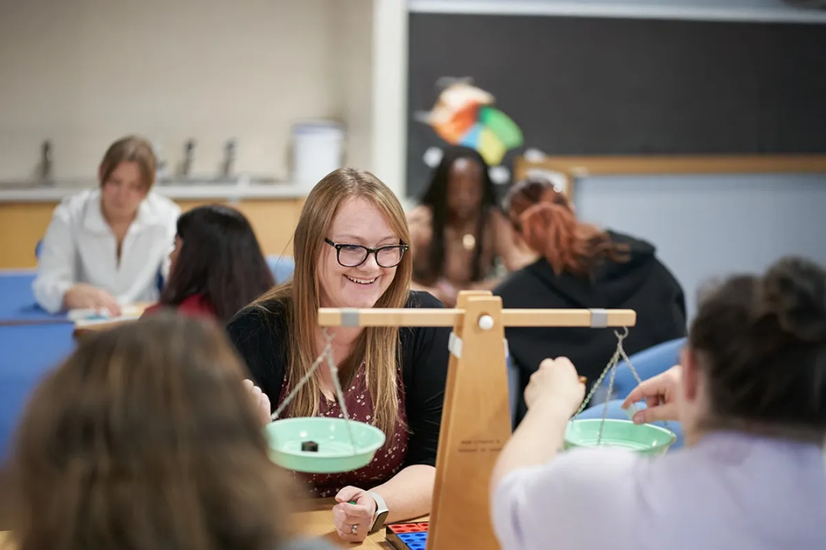 People take part in a classroom activity using a wooden balance scale and hands‑on learning materials.