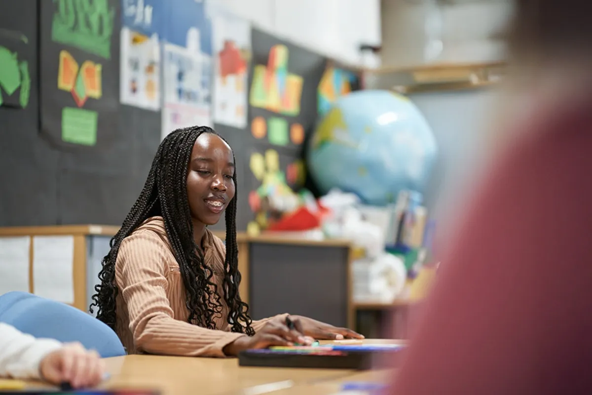 A person sits at a classroom table with colourful displays and a large globe in the background.