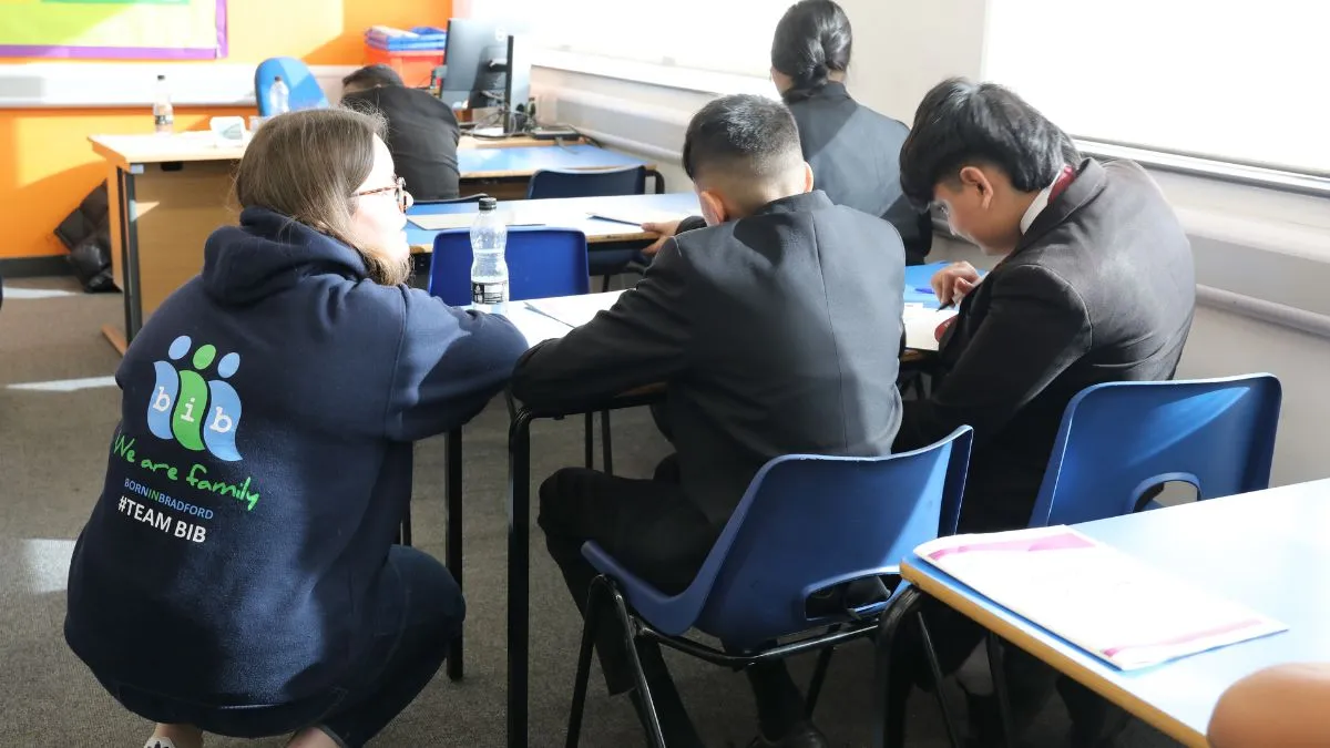A woman talks to school children sat at a table.