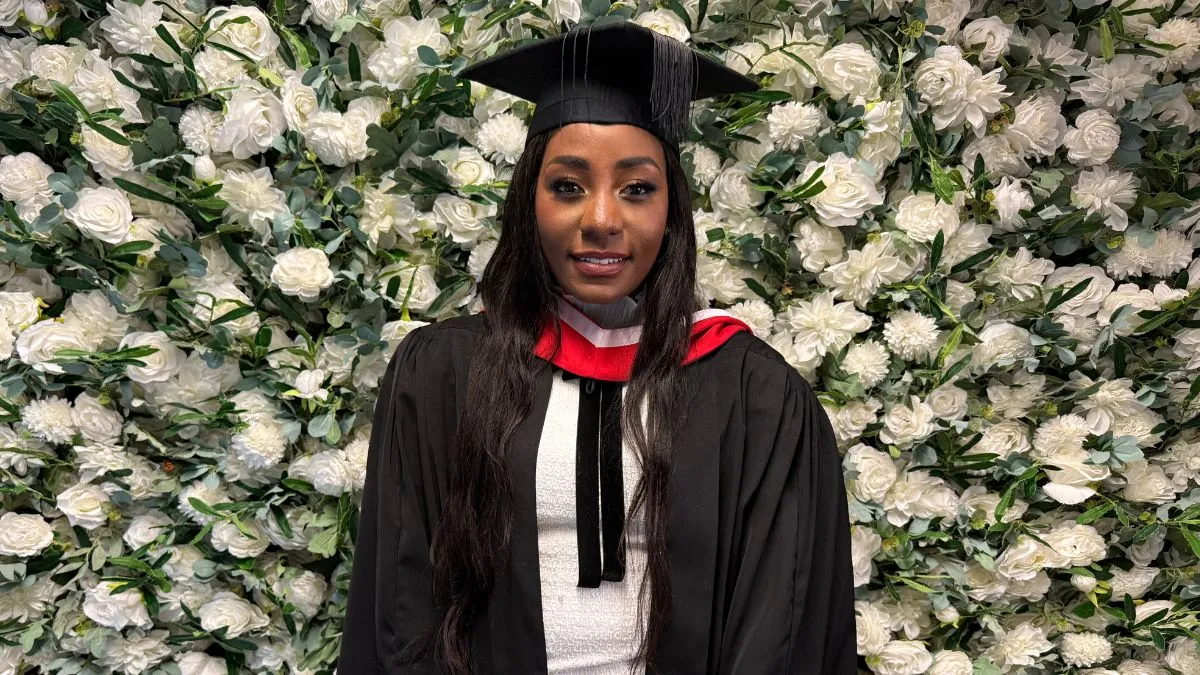 A female graduate poses for a picture in front of a white flower wall.