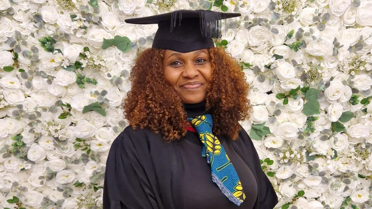 A graduate stand in front of a white flower wall.