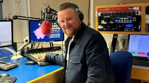 Man sitting in front of  a microphone in a radio studio.