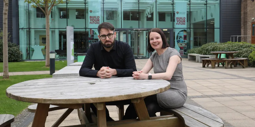 Man and women sat at table outside university building.