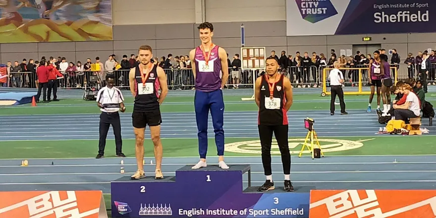 Three male athletes stand on podium.