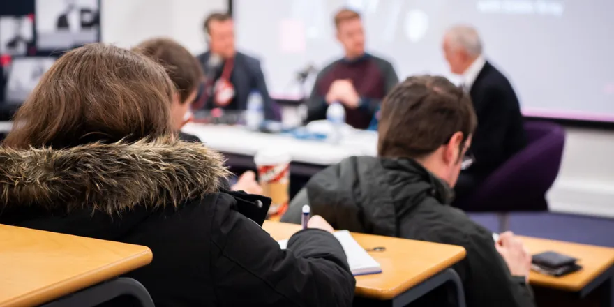 students in lecture theatre taking notes and listening to panel.