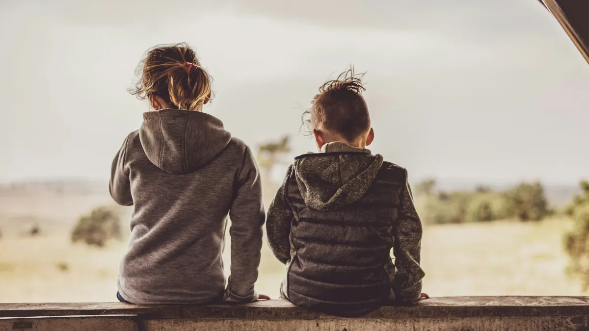Two children in dark grey clothing with their backs turned..
