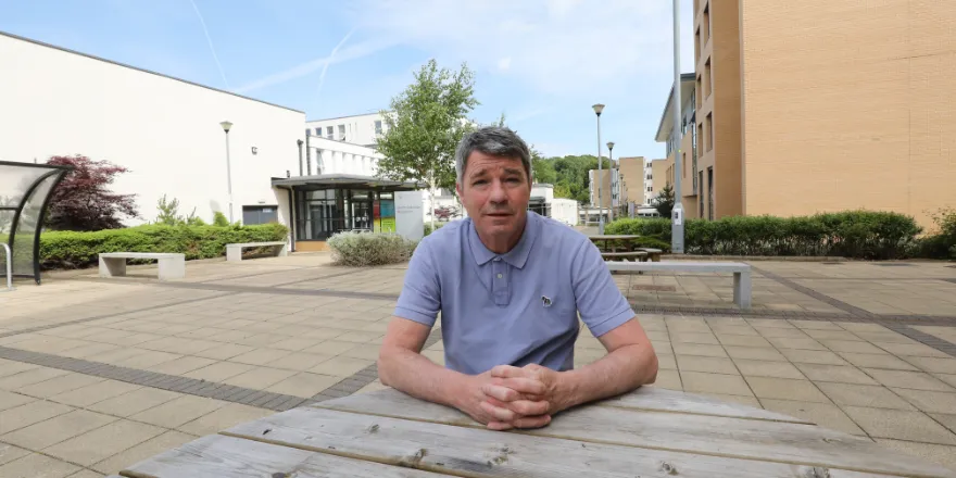 Man sat at table outside university building.