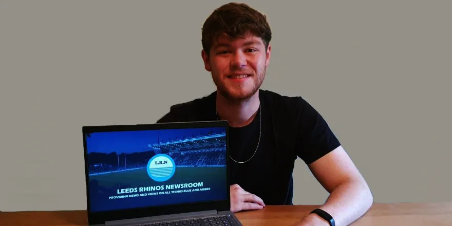 Male with black t-shirt and brown hair with laptop open on blue webpage.