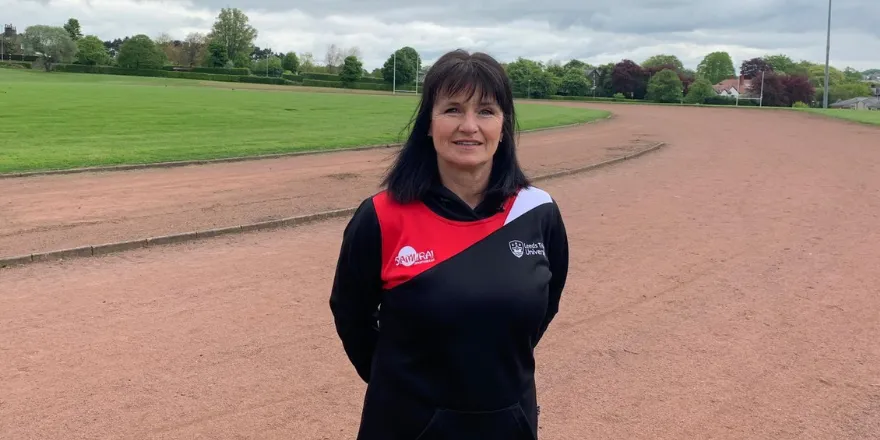 Female with black hair stands on running track wearing hoodie and joggers.