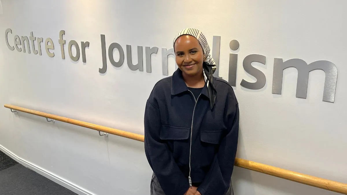 A student stands in front of a white wall displaying the words Centre for Journalism.