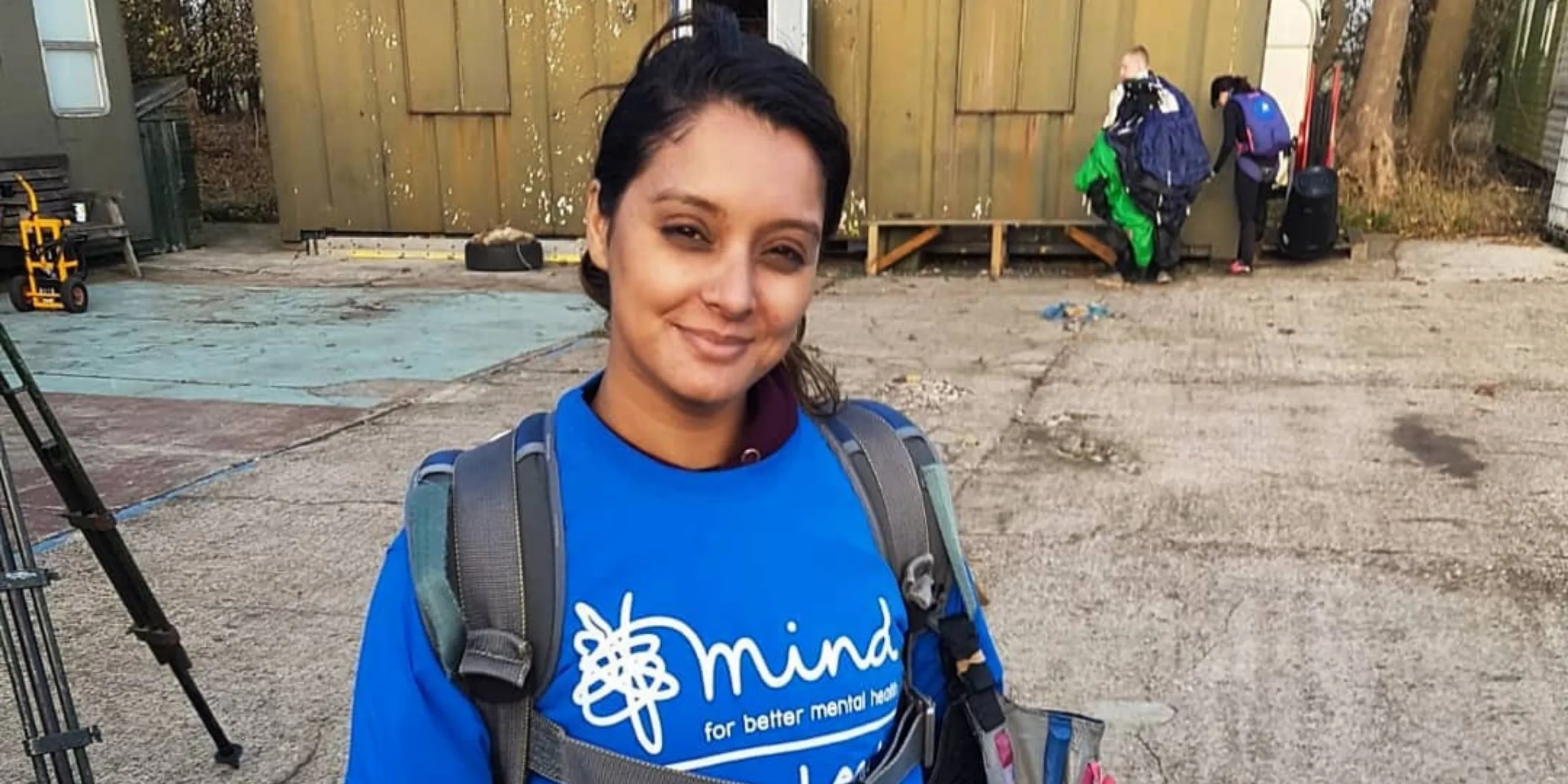 Woman with dark hair and backpack over her shoulders with blue Mind t-shirt on.