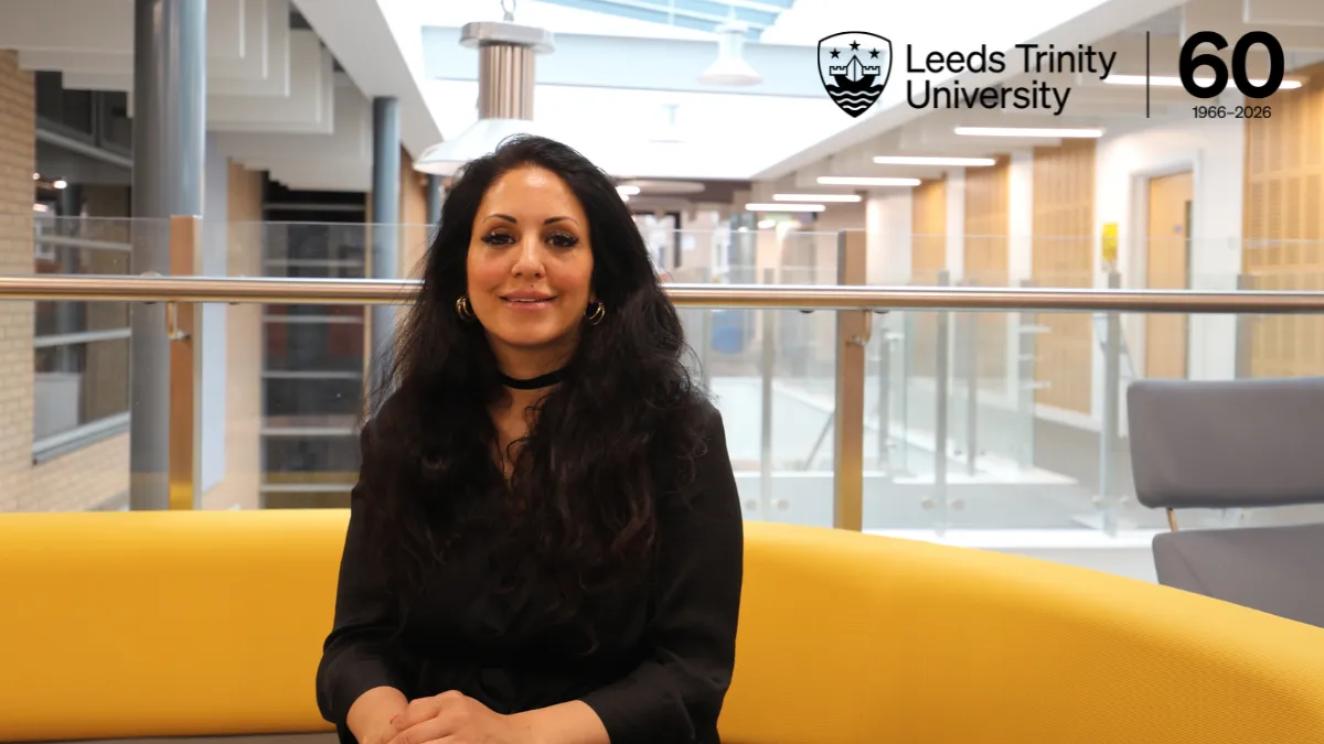 A female academic sitting on a yellow sofa and smiling. In the top right corner of the image, there is a black font logo reading Leeds Trinity University 60, 1966-2026..