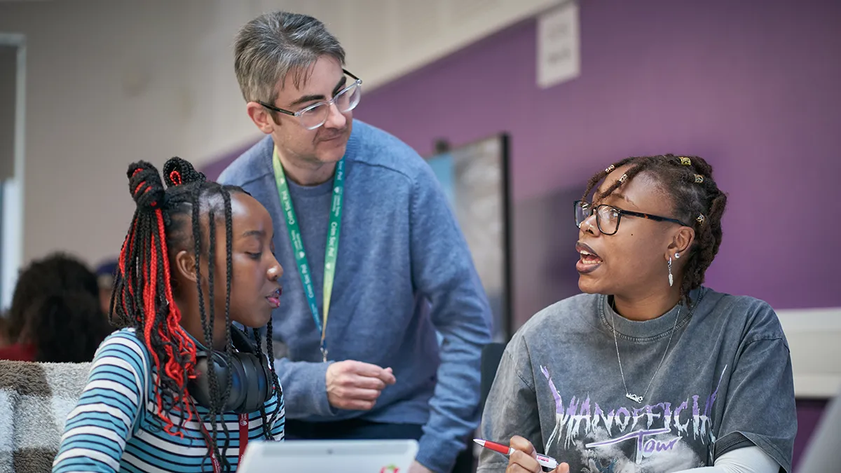 A lecturer talking to two students in a classroom at Leeds Trinity University..