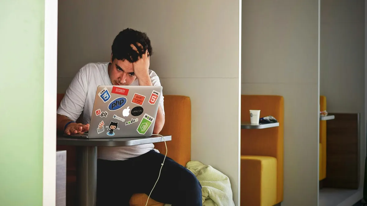 A student working on a laptop with his head rested on his arm..