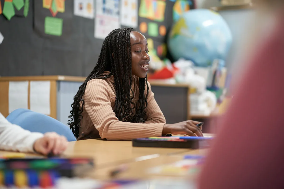 A student smiles while working on a colourful classroom activity at a table in an education seminar room..
