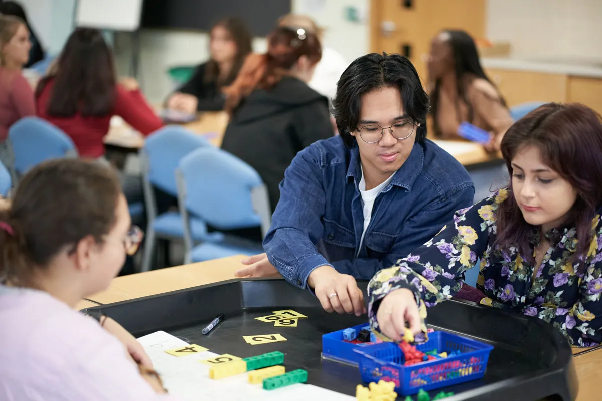 Two students work together at a classroom table, using number and counting blocks as part of a practical learning task..