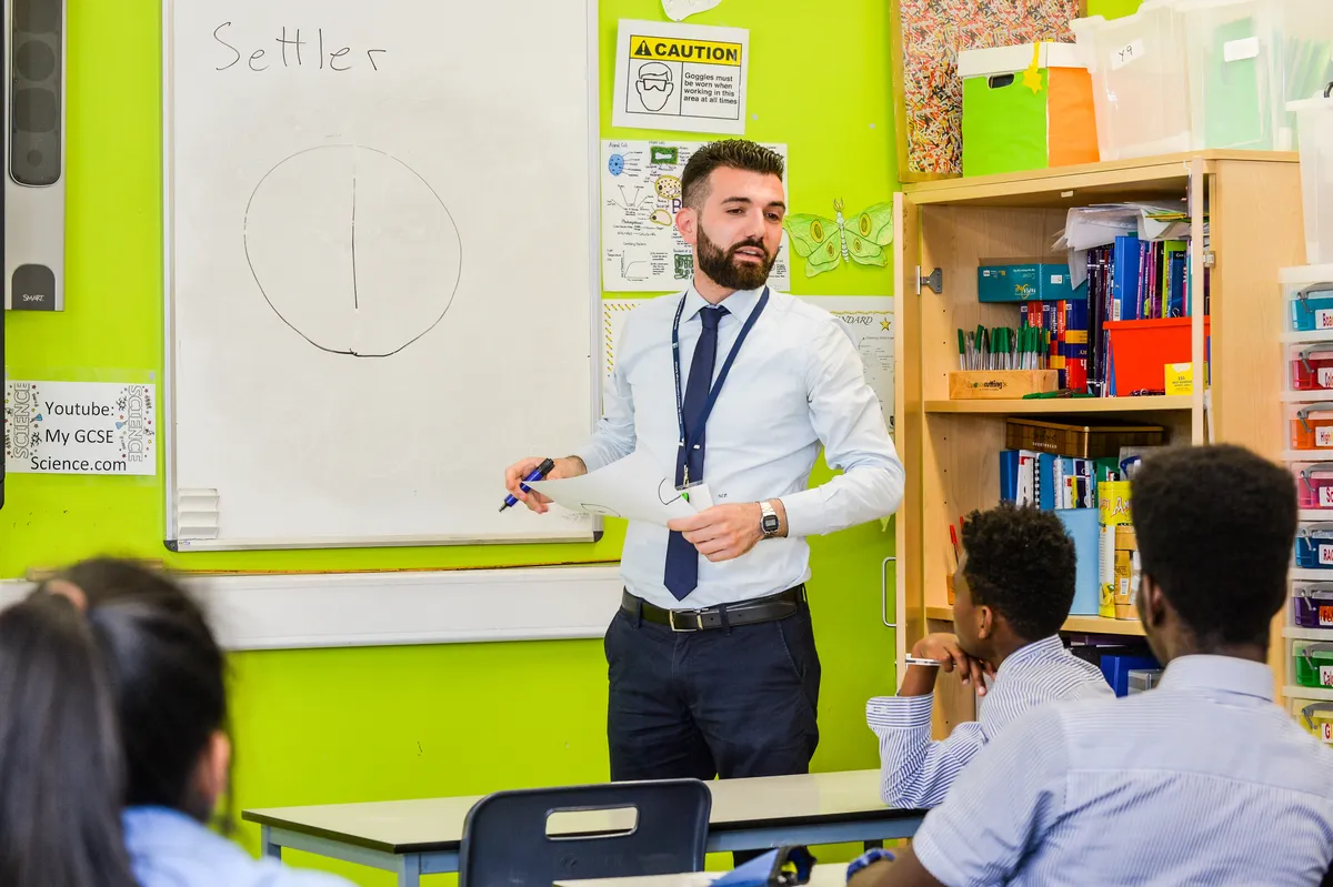 Male teacher standing in front of a white board teaching students.
