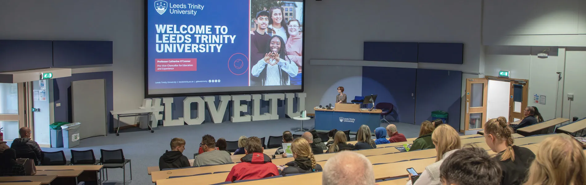 Families and prospective students sit in the auditorium listening to a presentation