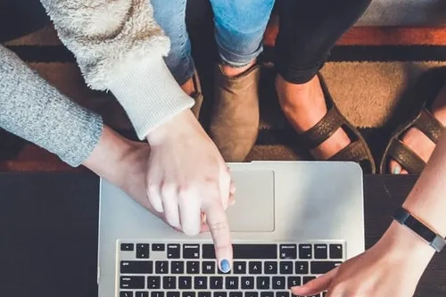 Three pairs of hands pointing to laptop.
