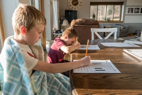 Children sitting at dinner table doing school work .