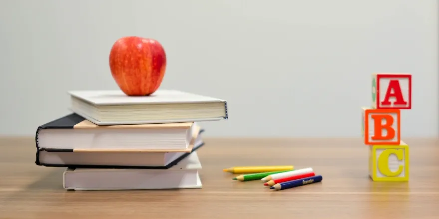 Brown desk with stack of books, red apple and colouring pencils.