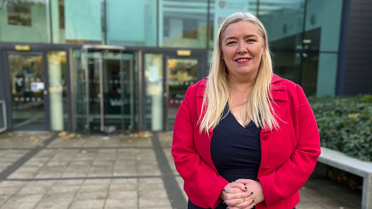 A female academic with long blonde hair and wearing a red jacket smiling..