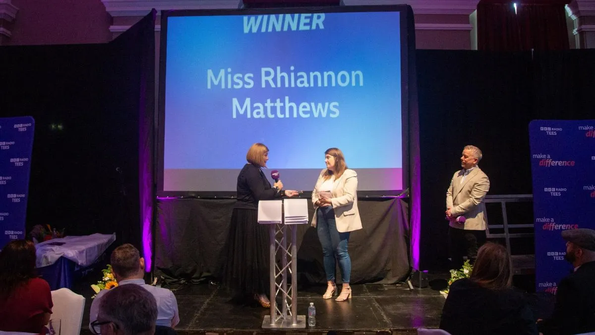 Three people stand on a stage at an awards ceremony.