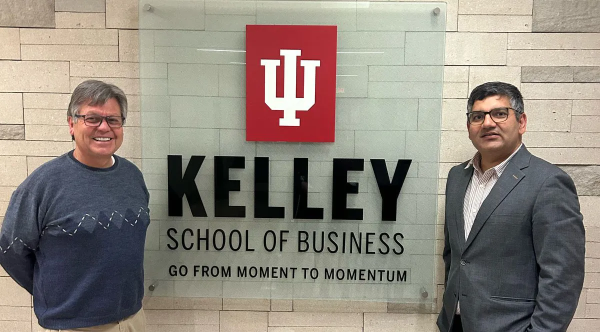 Two academics standing on either side of a sign that reads Kelley School of Business..