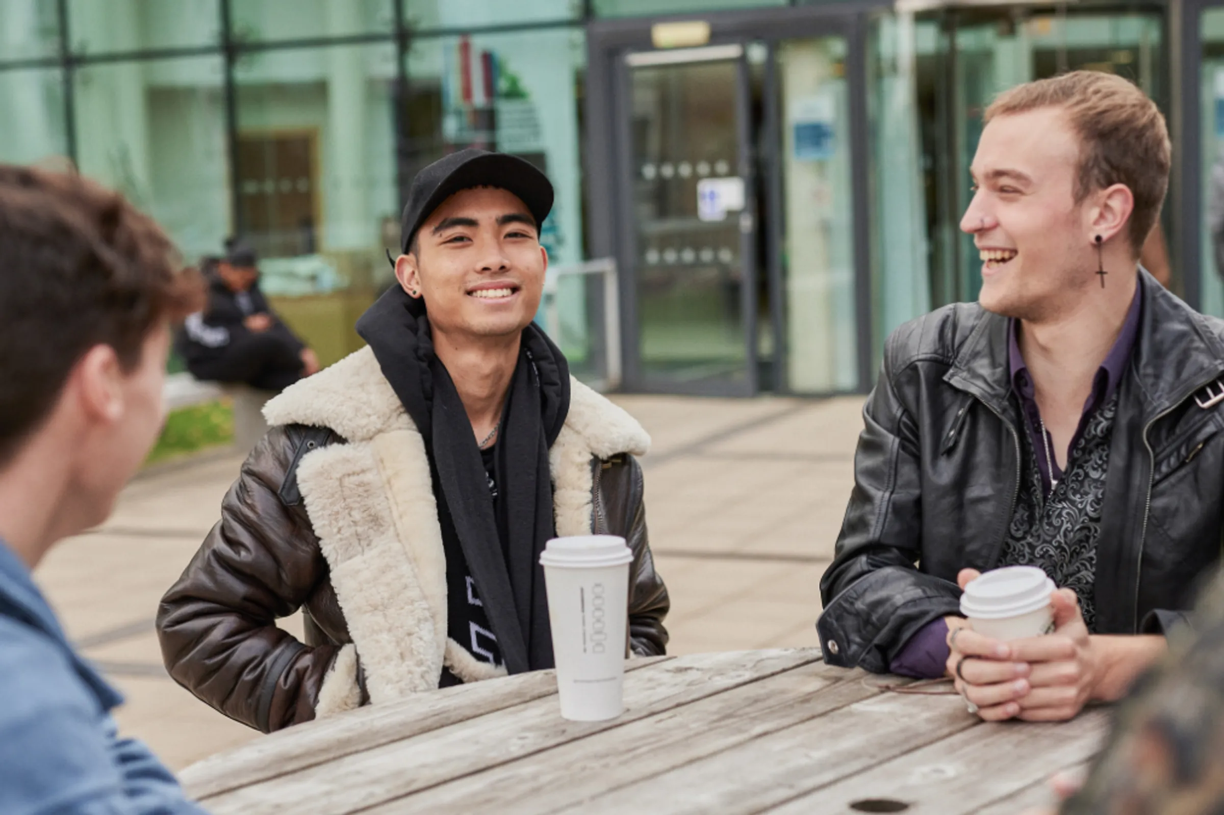 A group of students sitting around a wooden table, talking and drinking coffee.